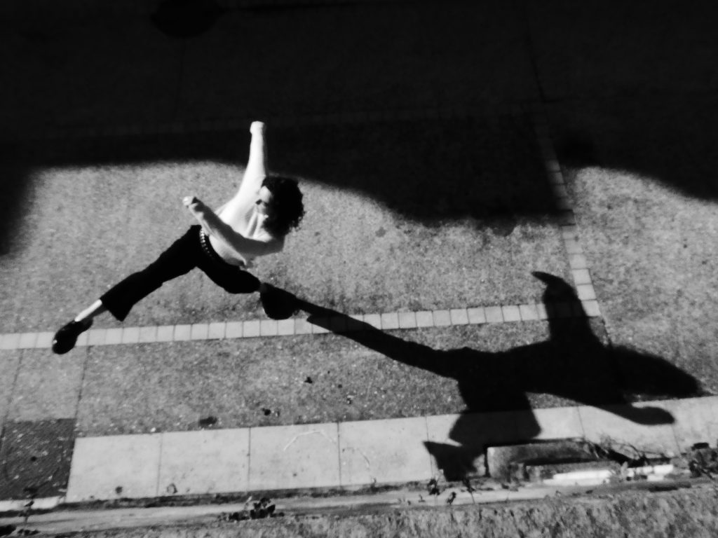 Photographie de rue en noir et blanc. Mouvement d'une danseuse corps entier et ombre